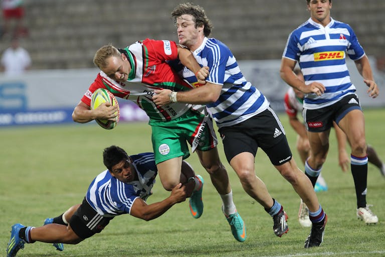 Rugby players in a fierce tackle during a live outdoor match, showing the physical intensity that makes head protection essential.