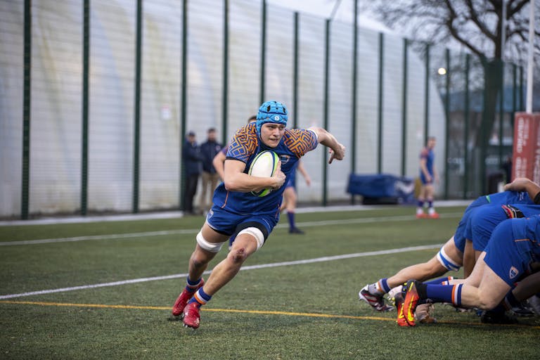 Rugby players in action wearing soft scrum caps during a match, illustrating rugby’s no-helmet safety approach.