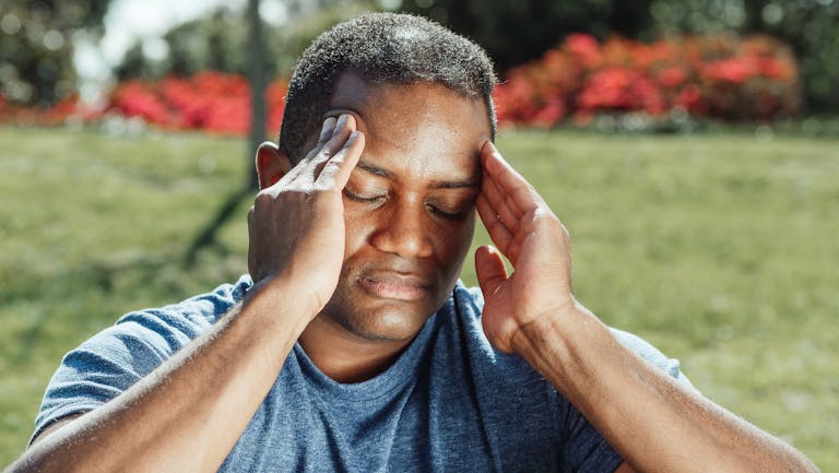 Man touching his temples with a headache, illustrating what to do in a concussion situation and early symptoms people often look for.